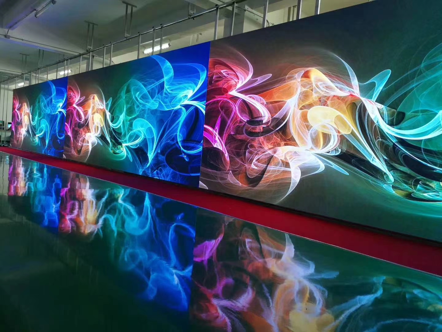 Curved indoor LED video wall displaying vivid flowing colour artwork, mirrored on a polished factory floor