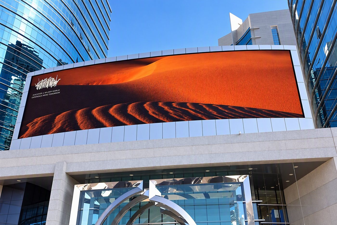 Curved outdoor LED media wall mounted on a modern glass building, showing a desert landscape