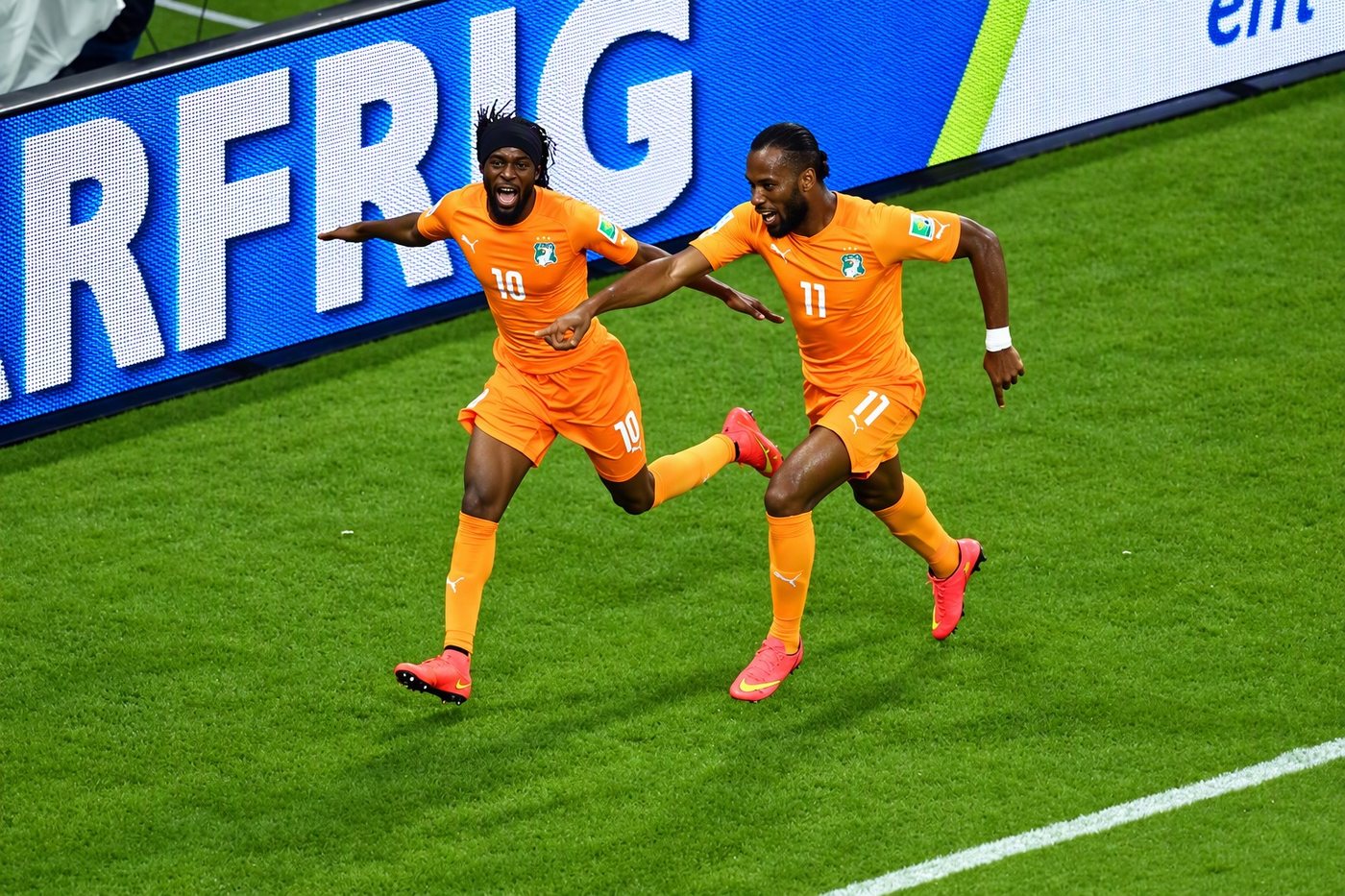 Footballers celebrating in front of a bright LED perimeter board at a stadium pitch